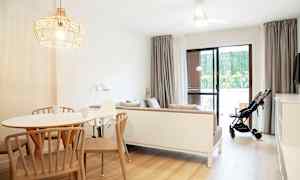 En lys og moderne innredet stue med et spisebord, en sofa og en barnevogn ved glassdøren. (AI-generert tekst)