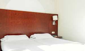 To enkeltsenger med hvitt sengetøy og en mørk trehodegavl. En vegglampe er montert på siden. (AI-generert tekst)