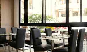 En restaurant med bord og stoler, med utsikt til en gårdsplass gjennom et stort vindu. (AI-generert tekst)