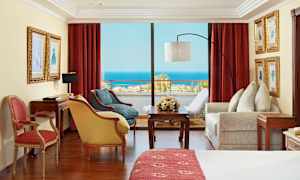 Rom med røde gardiner, møbler og utsikt over havet. (AI-generert tekst)