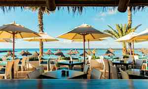 Uteservering ved stranden med parasoller og utsikt mot havet. (AI-generert tekst)