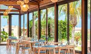 En restaurant med store vinduer og utsikt over palmer og planter. (AI-generert tekst)