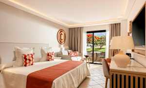 Et lyst og elegant hotellrom med en stor seng, dekorerte puter og et privat uteseteområde med utsikt over en hage. (AI-generert tekst)