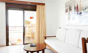 Interiør av et rom med en sofa, et bord og et maleri av seilbåter på veggen. Glassdør leder til en balkong. (AI-generert tekst)