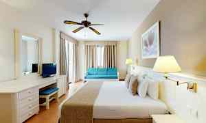 Et hotellrom med en dobbeltseng, skrivebord, sofa og takvifte. (AI-generert tekst)