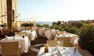 Bilde av en utendørs restaurant med dekkede bord og havutsikt. (AI-generert tekst)