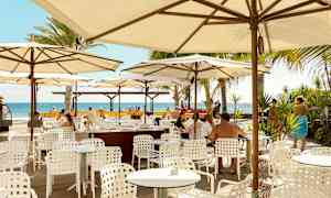 Utendørs restaurant med hvite bord og stoler under parasoller, utsikt mot havet. (AI-generert tekst)