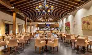 En restaurant med høyt trebjelketak, mange bord og stoler. Veggene er dekorert med kunstverk. (AI-generert tekst)