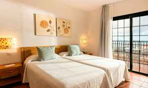 To enkeltsenger med hvitt sengetøy i et rom med utsikt mot en balkong. (AI-generert tekst)