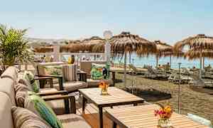 Uteplass med sittemøbler og bord med utsikt over en strand med parasoller og solsenger. (AI-generert tekst)