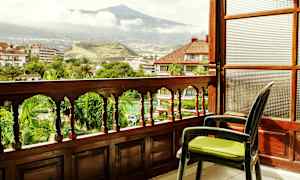 Utsikt fra en balkong med tre rekkverk som vender mot en grønn hage og et fjell i bakgrunnen. (AI-generert tekst)