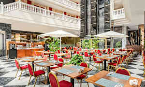 En restaurant med bord, røde stoler og parasoller i et lyst atrium. (AI-generert tekst)
