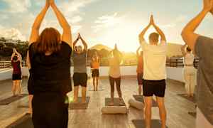 En gruppe mennesker utfører yogastillinger på en utendørsplattform ved solnedgangen. (AI-generert tekst)