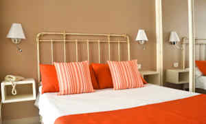 Et hotellrom med en seng kledd i hvite og røde sengeklær, omgitt av vegglamper. (AI-generert tekst)