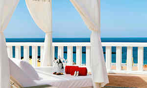 Solseng under hvitt baldakin med utsikt over havet, med håndkle og champagnekjøler. (AI-generert tekst)