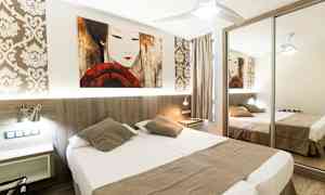 Et hotellrom med en dobbeltseng, speilgarderobe og dekorativ tapet. (AI-generert tekst)