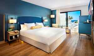 Hotellrom med dobbeltseng, sittemøbler og utsikt mot havet. (AI-generert tekst)