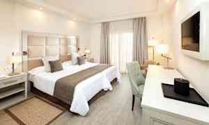 Et hotellrom med en dobbeltseng, skrivebord og stol. (AI-generert tekst)