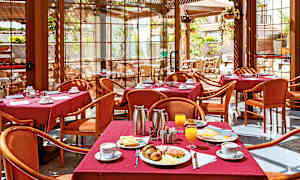 En restaurant med bord dekket med røde duker, serverer frokost inkludert kaffe, jus og bakverk. (AI-generert tekst)