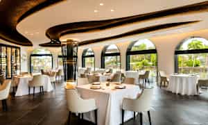 Restaurant med lys innredning, store vinduer og dekkede bord. (AI-generert tekst)