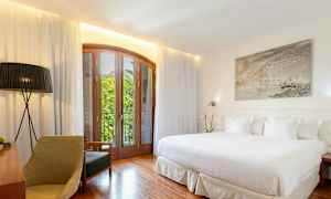 Et lyst hotellrom med en stor seng, tremøbler og en balkong med utsikt. (AI-generert tekst)