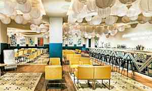 En moderne og innbydende restaurant med gule lenestoler, dekorative lanterner i taket og en stilren bar. (AI-generert tekst)