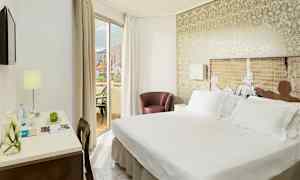 Et hotellrom med dobbeltseng, et skrivebord med lampe og en balkong med utsikt. (AI-generert tekst)