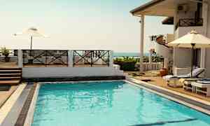 Utendørsbasseng ved et feriekompleks med solsenger og parasoller samt utsikt over havet. (AI-generert tekst)