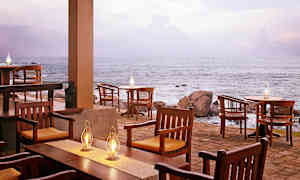 En uteservering ved havet med trestoler og bord, og flere fotogenlamper som lyser. (AI-generert tekst)