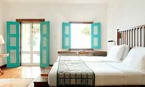 Et lyst soverom med en stor seng, hvitt sengetøy og turkise skodder som slipper inn naturlig lys. (AI-generert tekst)