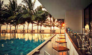 En uteservering ved et basseng med utsikt over stranden og palmer ved solnedgang. (AI-generert tekst)