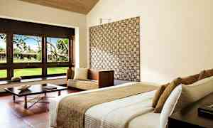 Moderne innredet hotellrom med seng, sofamøbel og store vinduer som vender mot en frodig hage. (AI-generert tekst)