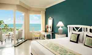 Hotellrom med havutsikt, innredet med en stor seng, skrivebord, stol og terrassemøbler. (AI-generert tekst)