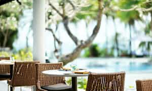 Et dekket bord med stoler utendørs ved et basseng, omgitt av trær og vegetasjon. (AI-generert tekst)