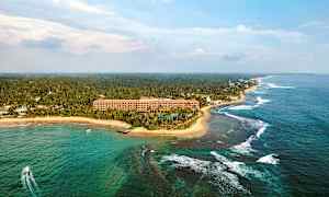 Luftfoto av en tropisk kystlinje med et hotell ved stranden, omgitt av palmer og hav. (AI-generert tekst)