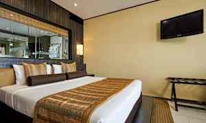 Et hotellrom med en dobbeltseng dekorert med brune og gyldne pyntegjenstander. En TV henger på veggen til høyre. (AI-generert tekst)