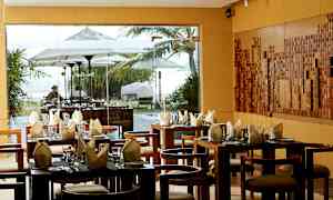 En restaurant med dekkede bord og utsikt gjennom vindu mot et utendørsmiljø med parasoller og vegetasjon. (AI-generert tekst)