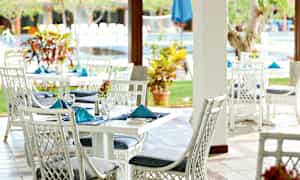 Et uterom med hvite rottingstoler og bord, dekorert med blå servietter, og planter i bakgrunnen. (AI-generert tekst)