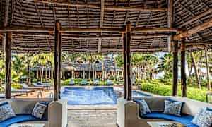 Utsikt fra et overbygd sitteområde med blå sofaer mot et basseng og omkringliggende grønne områder. (AI-generert tekst)