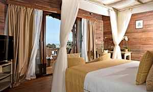 Et soverom med trepaneler på veggene, store vinduer med gardiner og utsikt mot havet. Rommet har en seng og en sittegruppe. (AI-generert tekst)