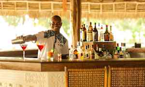 En bartender heller opp drinker i cocktailglass ved en bar. (AI-generert tekst)