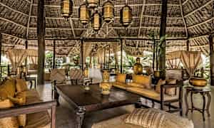 Et møblert og dekorert åpent område med trebord, sofaer og lykter under et vakkert stråtak. (AI-generert tekst)