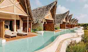 Bildet viser en rekke villaer med halmtak, som har private bassenger foran, omgitt av vegetasjon. (AI-generert tekst)