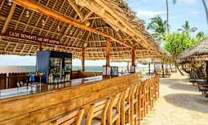 Strandbar med trebord og stoler under tak laget av palmeblader. (AI-generert tekst)