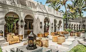 En utendørs terrasse med buer, palmer og sitteplasser inspirert av arabisk design. (AI-generert tekst)