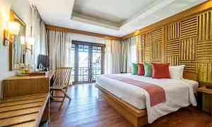 Et hotellrom med en dobbeltseng, puter i ulike farger, et trebord med stol og en balkong med utsikt. (AI-generert tekst)