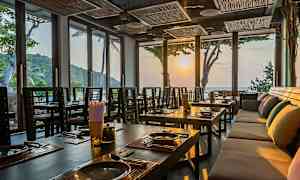 Interiør av en restaurant med dekkede bord og store vinduer som slipper inn lyset fra solnedgangen. (AI-generert tekst)