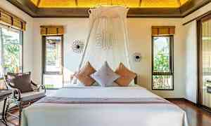 Et soverom med en stor seng dekorert med puter og en hvit baldakin. Rommet har vinduer med utsikt mot grønt. (AI-generert tekst)