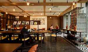 Interiør av en kafé eller arbeidsområde med tremøbler, dekorasjoner på bordet og personer som arbeider eller samtaler. (AI-generert tekst)