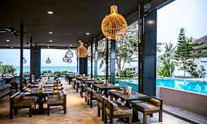 En utendørs restaurant med sitteplasser ved et basseng, med havet i bakgrunnen. (AI-generert tekst)